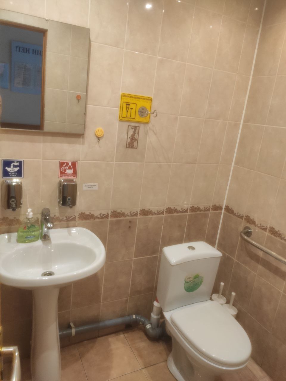 туалетная комната, в которой имеется держатель для одежды и костылей с тактильной табличкой шрифта Брайля, а так же поручень